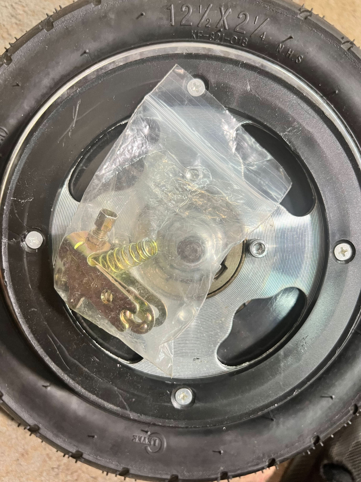 Rear Wheel Assembly with Wire Spoke Rim for the Razor Pocket Mod (Versions 13-30) (Blemished) showing wheel with plastic bag and metal spring on top, close-up of screws.