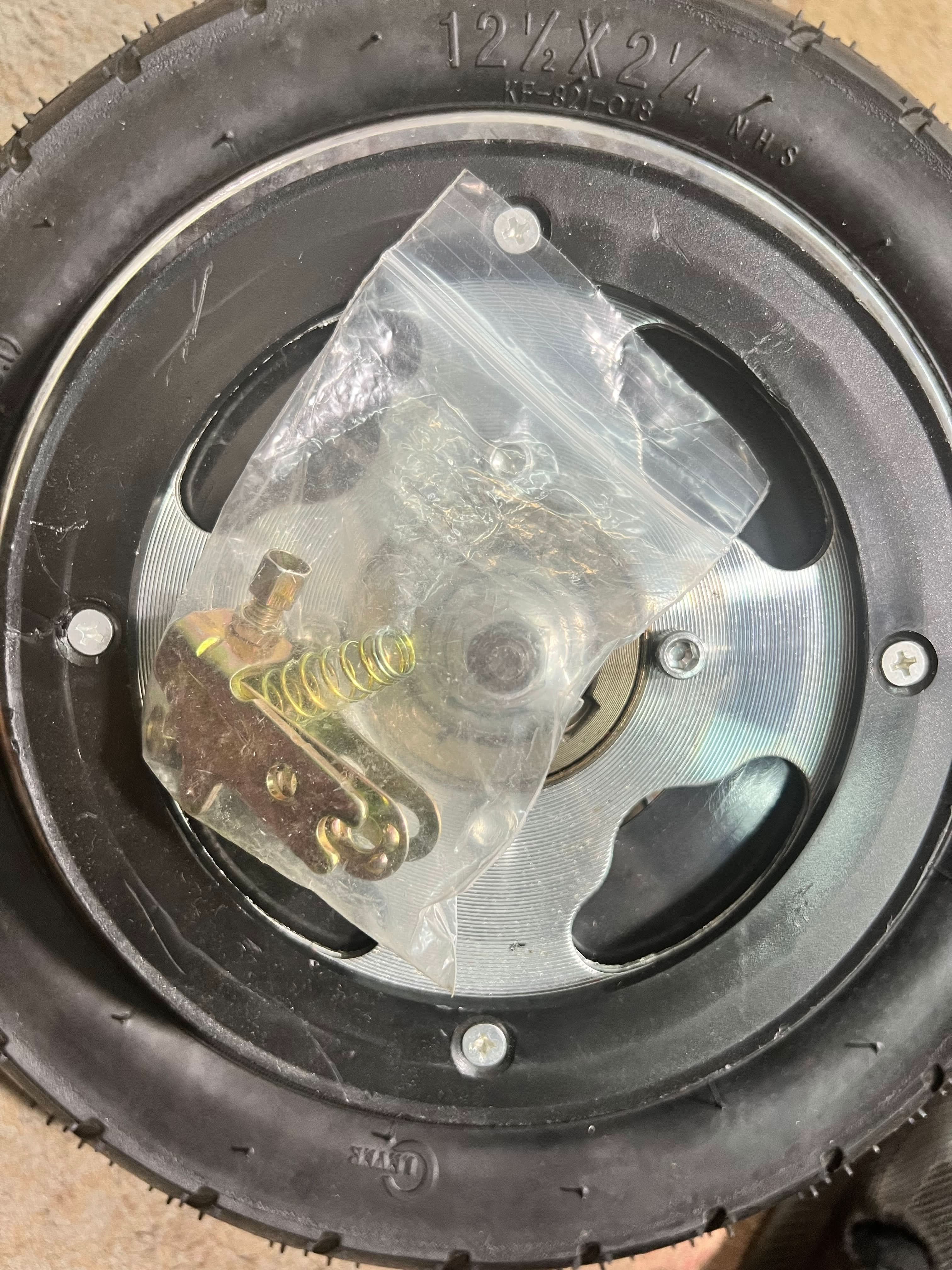 Rear Wheel Assembly with Wire Spoke Rim for the Razor Pocket Mod (Versions 13-30) (Blemished) showing wheel with plastic bag and metal spring on top, close-up of screws.