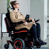 Woman seated in a power wheelchair with a joystick controller mounted on the armrest