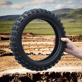 Hand holding a 2.50-10 Tire for the Razor SX500 McGrath Dirt Rocket, displaying its tread pattern over a dirt field background.